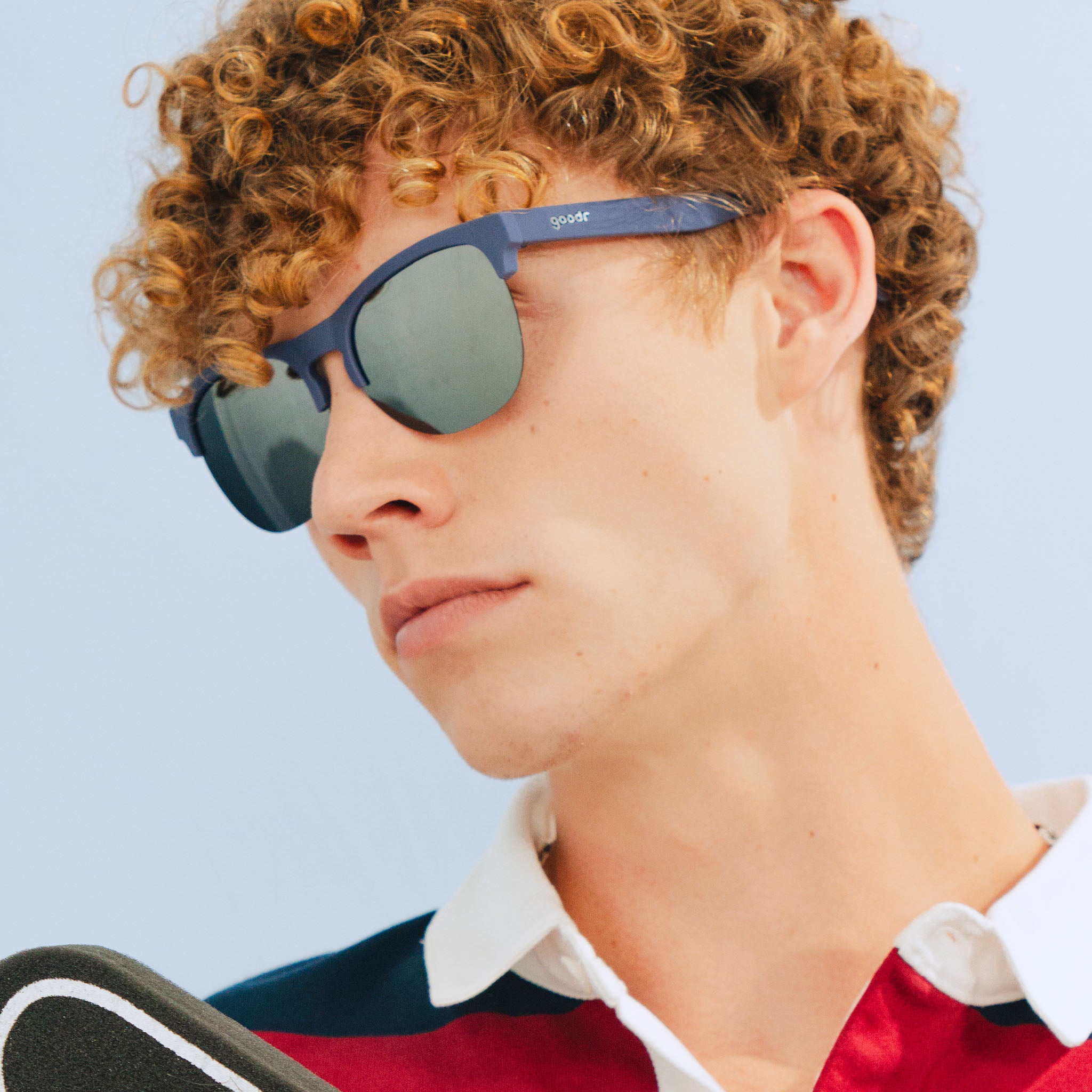 A stylish man wearing sleek navy blue half-rim sunglasses with polarized chrome reflective lenses looks off.