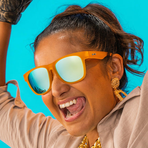 A woman wearing square sunglasses with orange frames and reflective blue lenses.