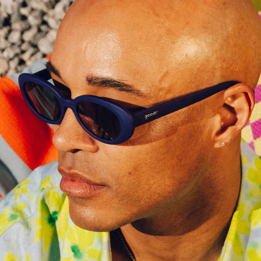 Three-quarter profile view of a bald man wearing a pair of deep purple, oval-shaped sunglasses with reflective lenses and a floral shirt.