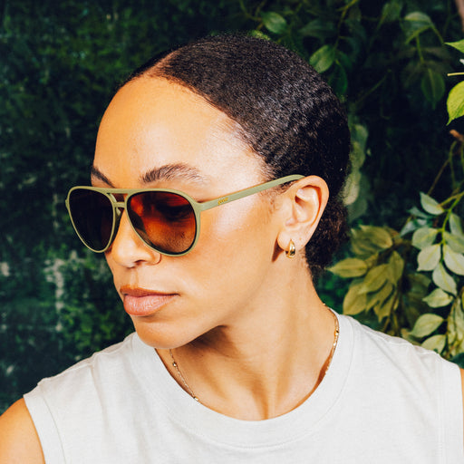 Side profile of a woman wearing green aviator sunglasses with amber gradient lenses.