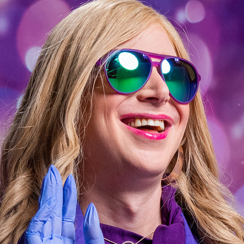 A woman wearing purple aviator sunglasses with green lenses looks off to the side, smiling.