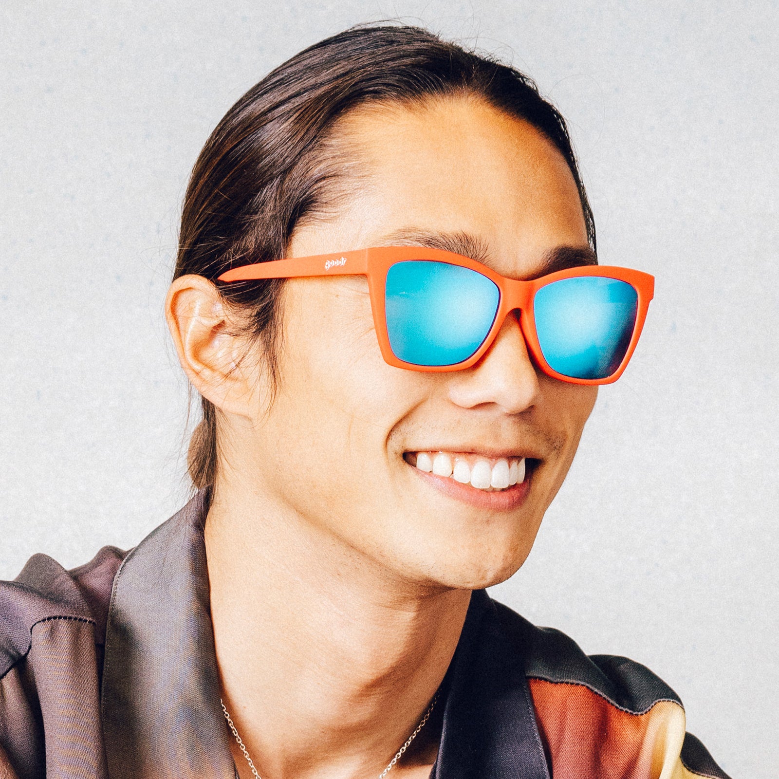 Side profile of a smiling man wearing red angular sunglasses with blue reflective lenses.