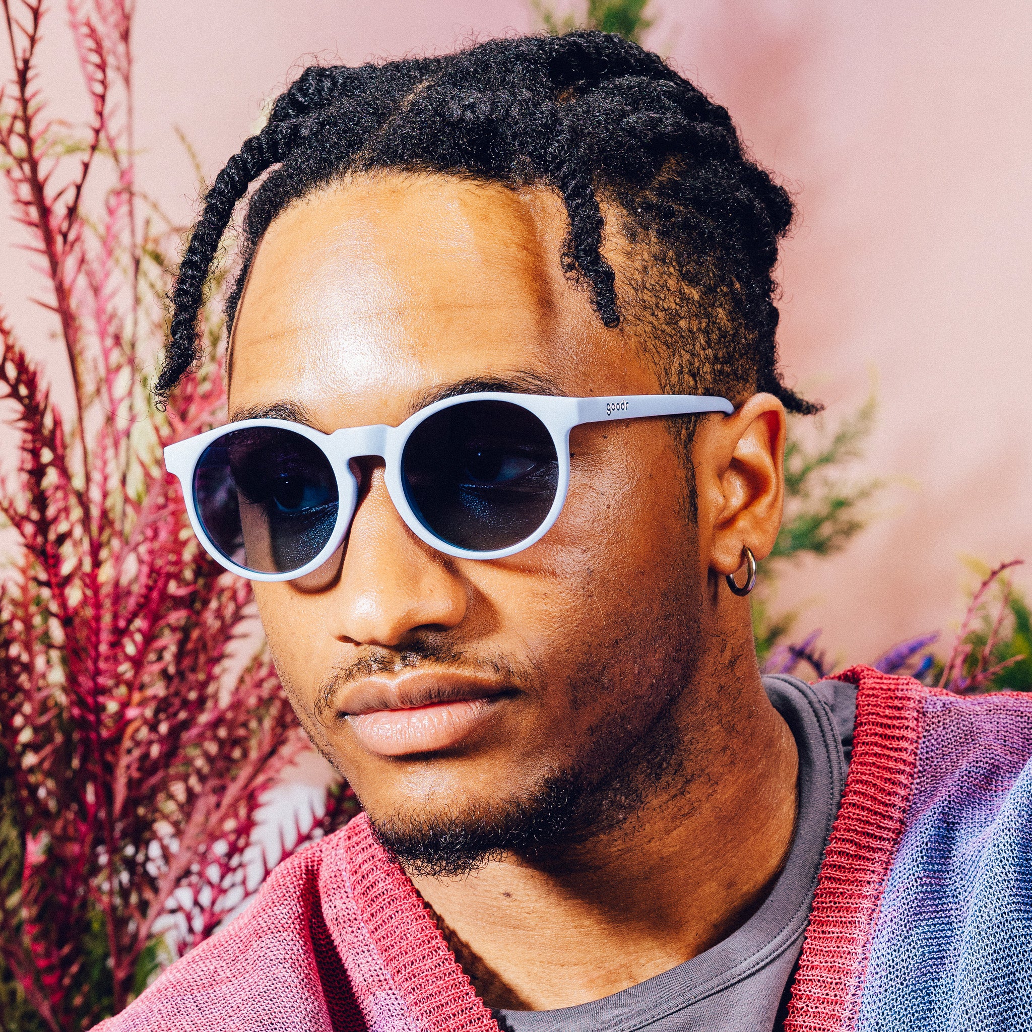 Front view of a man wearing light blue circular sunglasses with dark blue gradient lenses in front of a meadow backdrop.