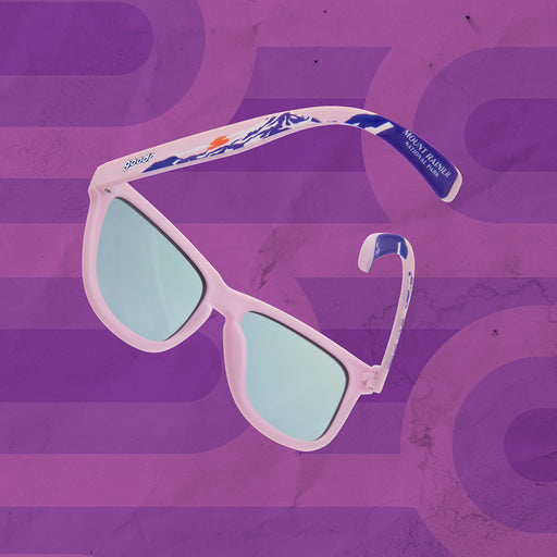 A pair of white-framed sunglasses with blue accents and reflective lenses, floating against a textured purple background. The arms of the sunglasses feature a blue mountain-themed design with the "goodr" logo.