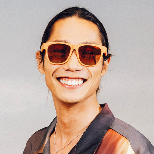 Portrait of a man smiling wearing large brown sunglasses with orange-gold ocean gradient lenses.
