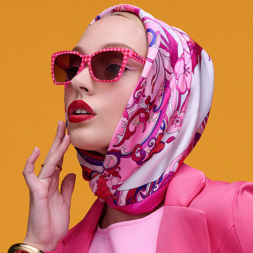 A woman in a Pucci-style silk scarf, matte red lips, and elegant pink clothes wearing red and pink houndstooth Pop Gs shades.