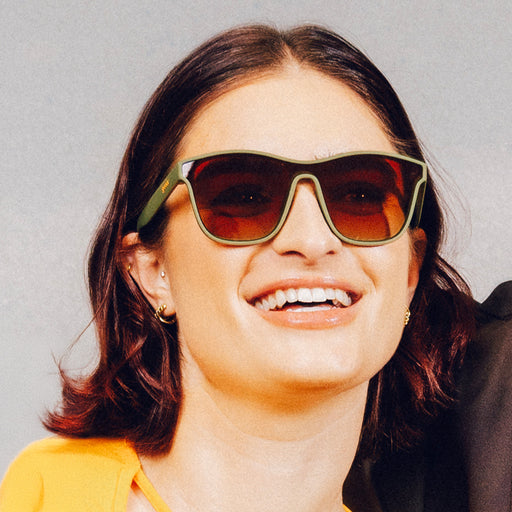 Smiling woman wearing green one-lens sunglasses with orange-gold ocean gradient lenses.