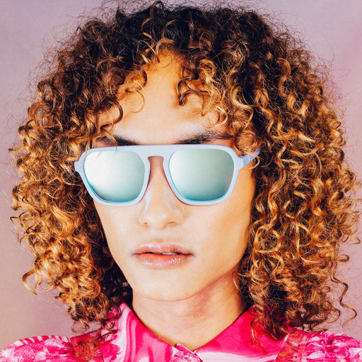 Front profile of a woman wearing light blue retro-inspired aviator sunglasses with blue reflective lenses.