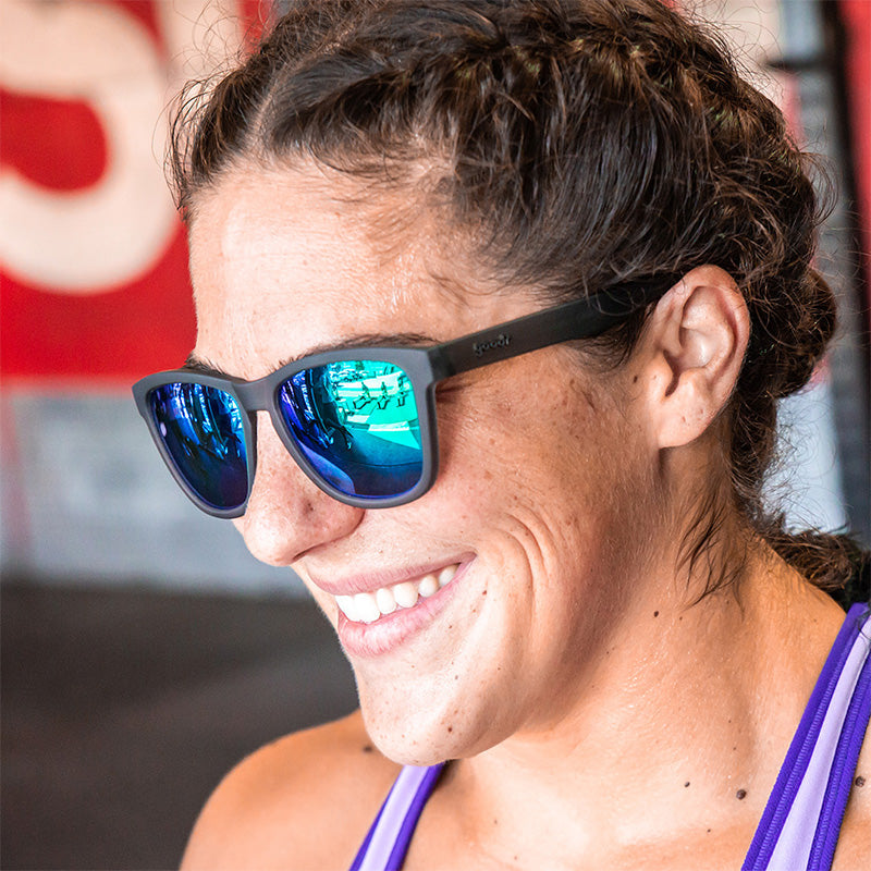 A woman wearing gray sunglasses with polarized green reflective lenses, smiling as she looks off to the side.