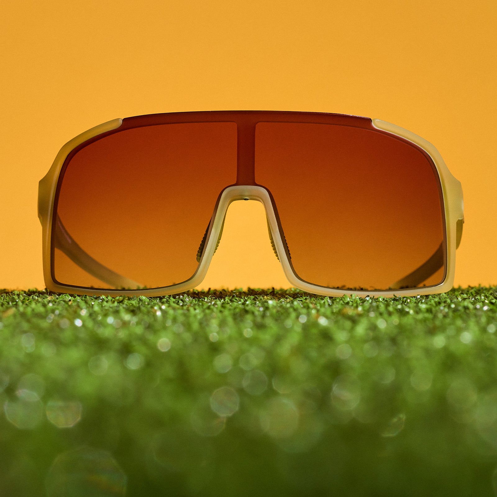 Translucent chartreuse wrap sunglasses with a rose gradient shield lens sitting on turf.