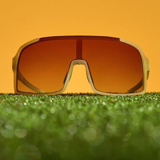 Translucent chartreuse wrap sunglasses with a rose gradient shield lens sitting on turf.