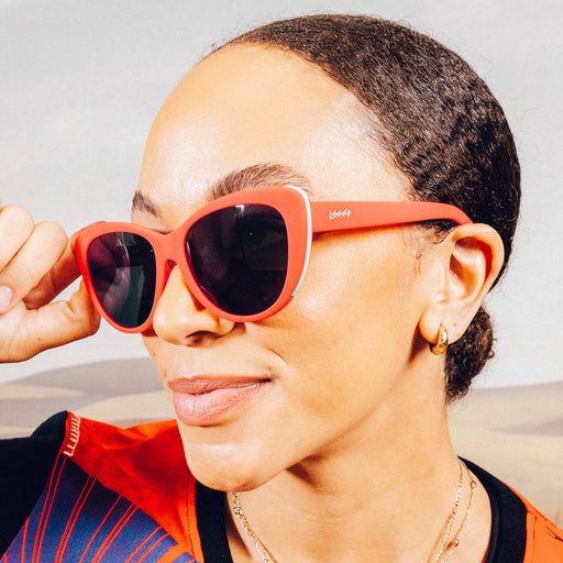 Woman smiles and poses while wearing red cat-eye sunglasses with black non-reflective lenses.