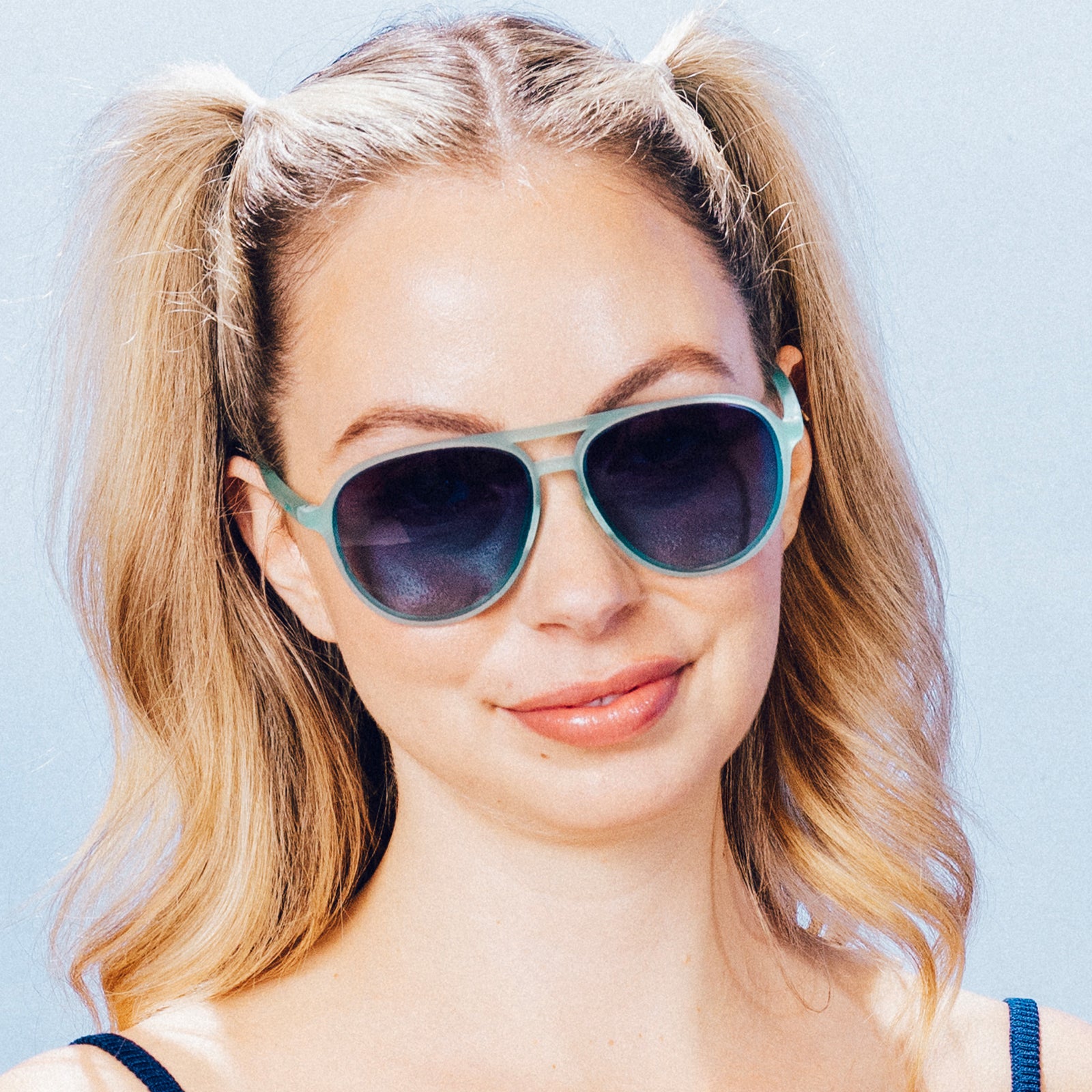 Front view of woman wearing translucent teal aviator sunglasses with dark blue gradient lenses.