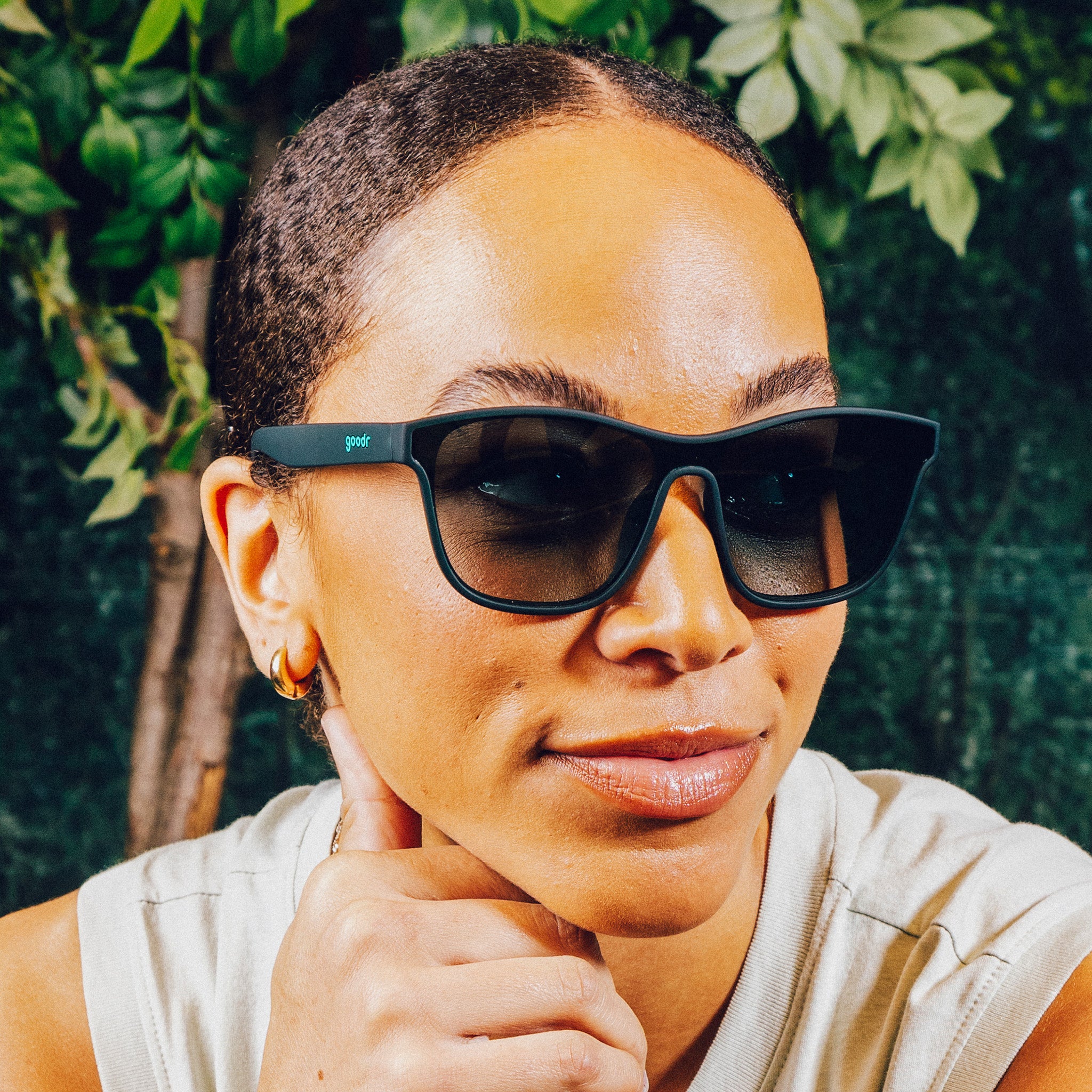 Profile view of woman wearing translucent teal one-lens sunglasses with green gradient lenses in front of a nature backdrop.