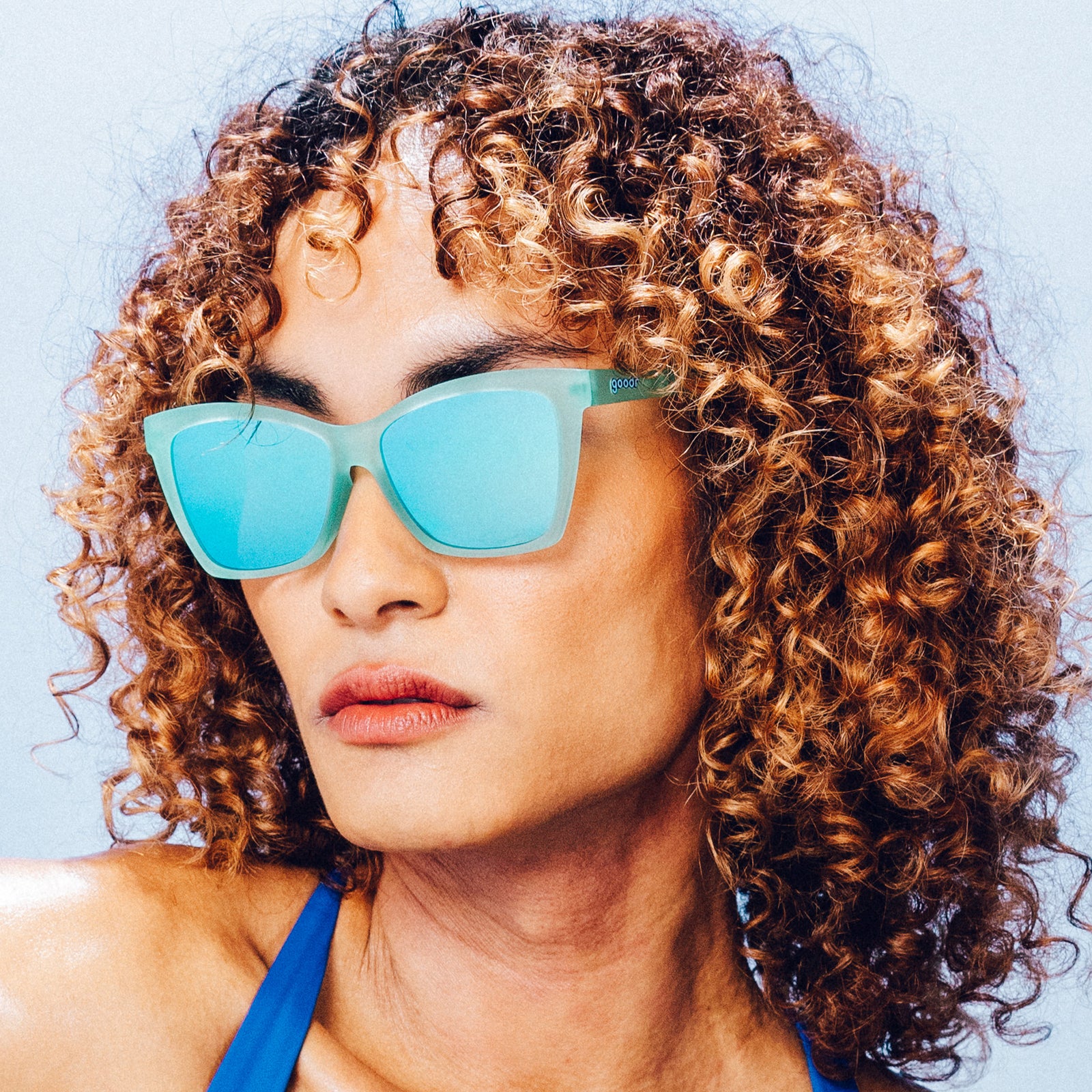 Front view of a woman wearing translucent angular sunglasses with reflective teal lenses.
