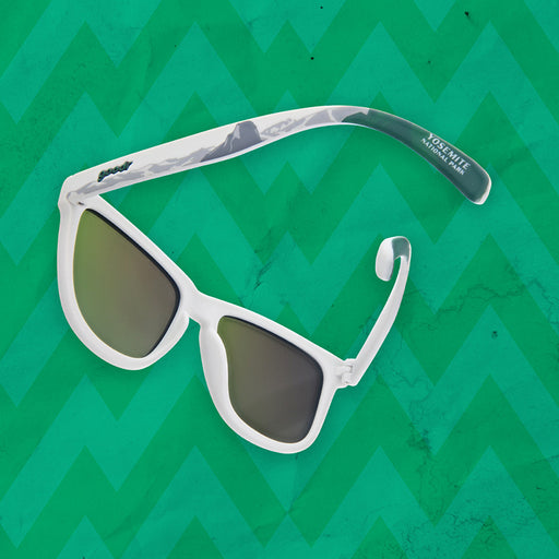 A pair of white sunglasses on a green background that have "Yosemite National Park" on the temples, as well as a silhouette of rocky mountains along the temples.