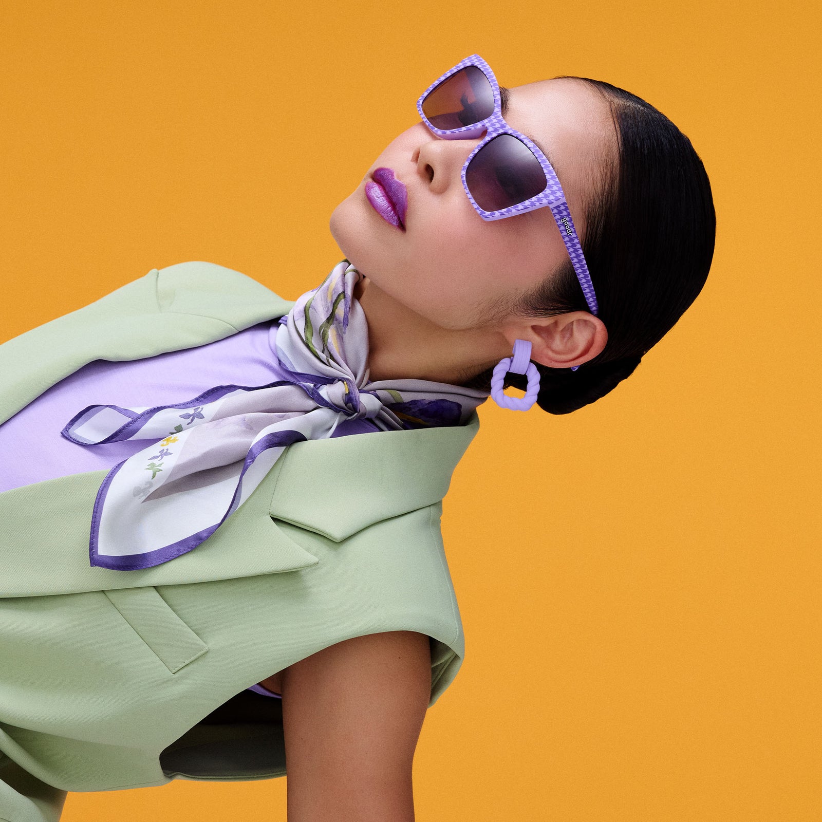 A fashionable woman, dressed in lavender and mint, is displayed diagonally, wearing purple houndstooth-print Pop Gs.