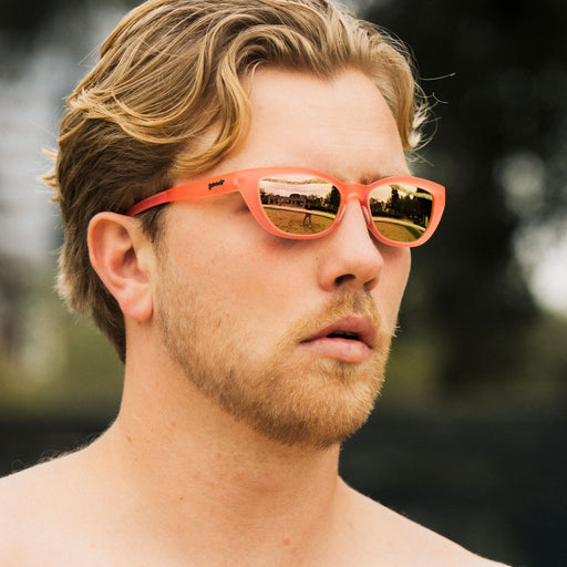 A  close-up of a blonde man with facial hair wearing a pair of translucent pink cat-eye Cheetah G glasses outdoors.