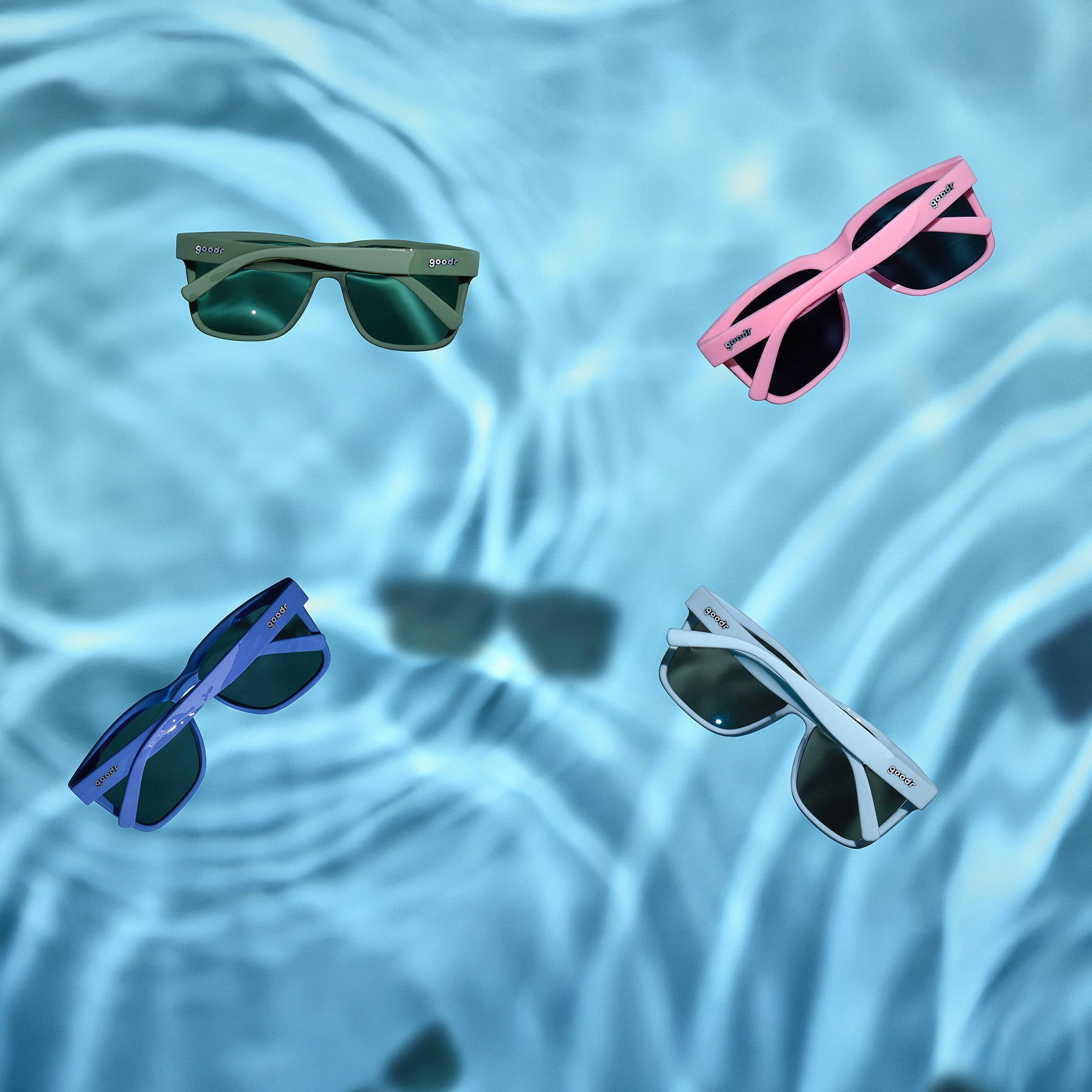 Four pairs of sunglasses floating in clear blue water.